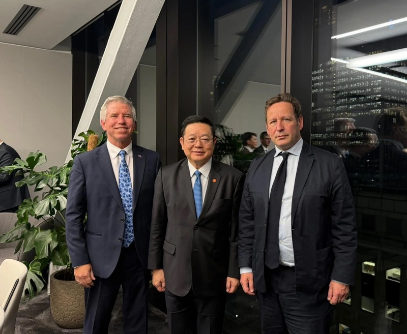 Three men standing together in a London office at night, with the city lit behind them